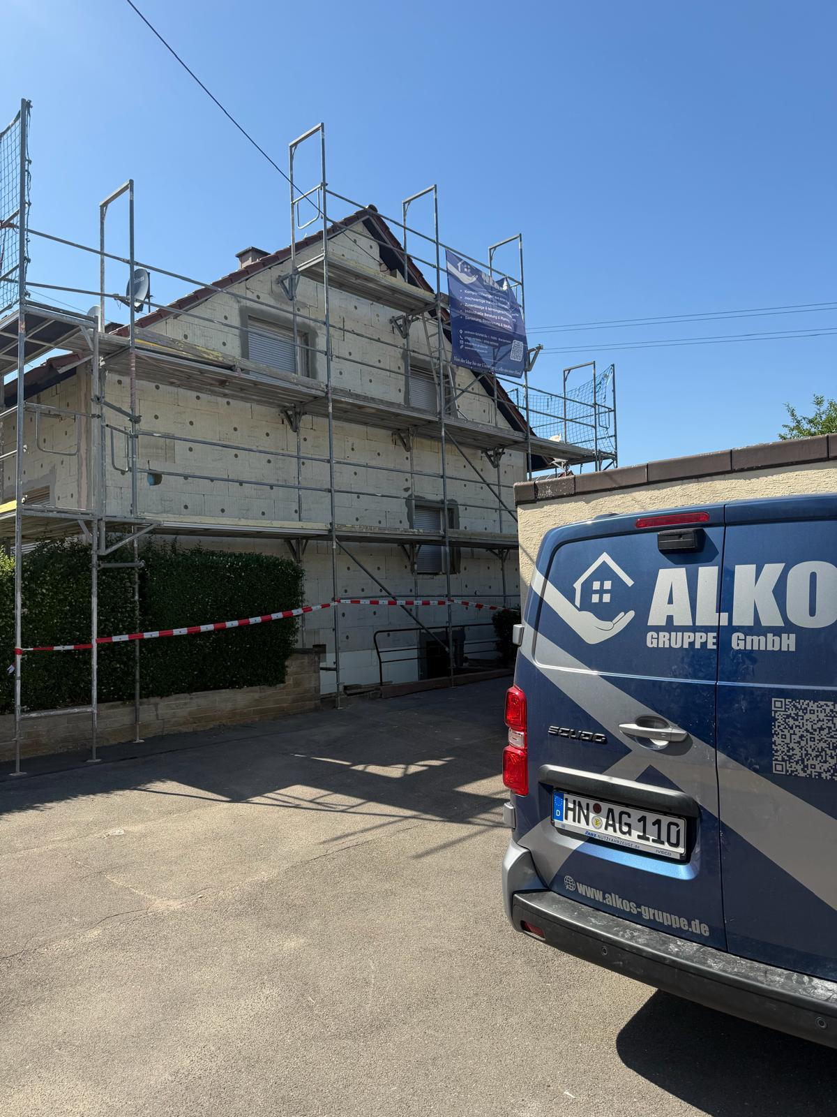 Eingerüstetes Mehrfamilienhaus mit Fahrzeug der ALKOS Gruppe davor